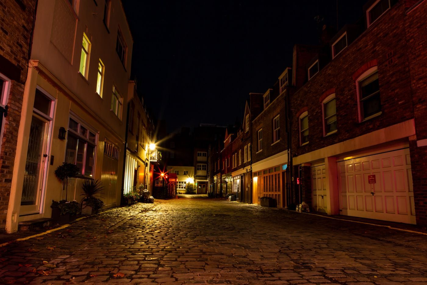 Quiet cobbled London mews at night lit by warm street lamps