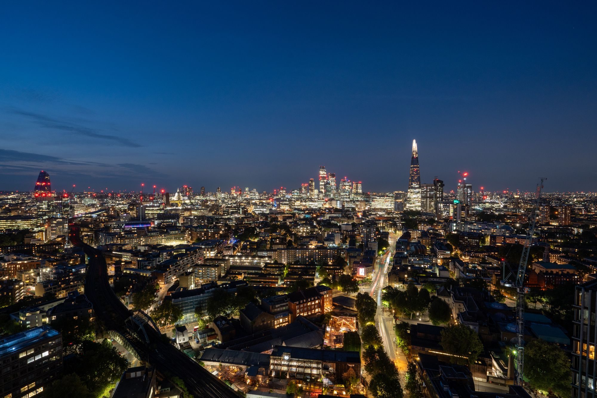 London at night from above, the Shard and City towers lit up over dark streets