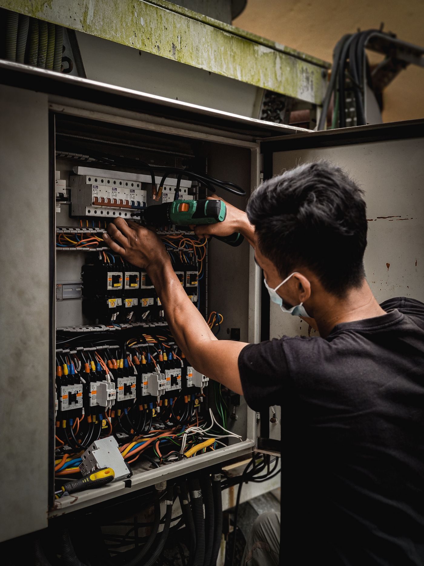 Electrician working inside an open distribution board full of breakers and wiring